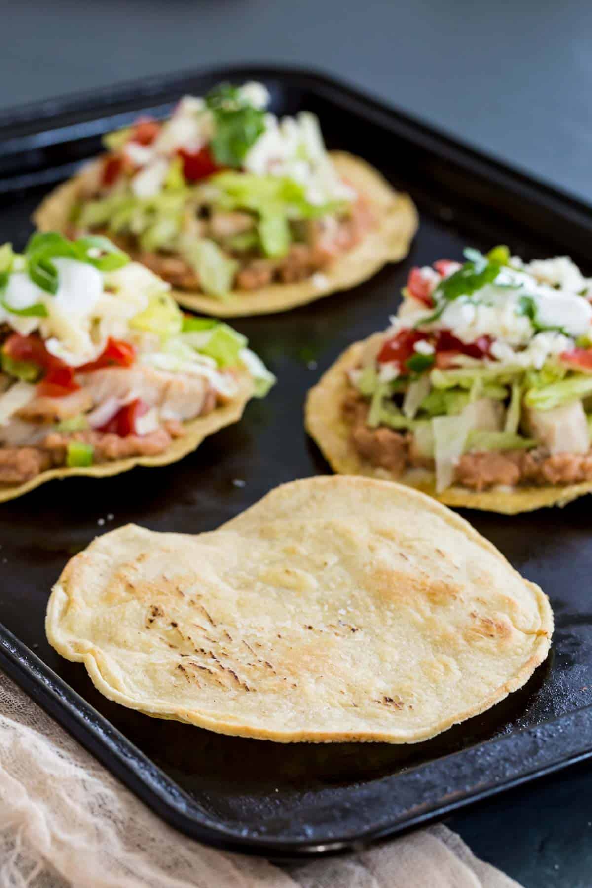 tostada shells on a baking sheet, one without toppings and three tostadas with the toppings on them