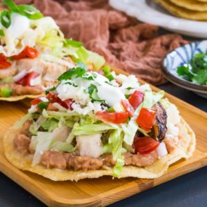 one chicken tostada topped with lettuce, tomatoes, and sour cream on a plate