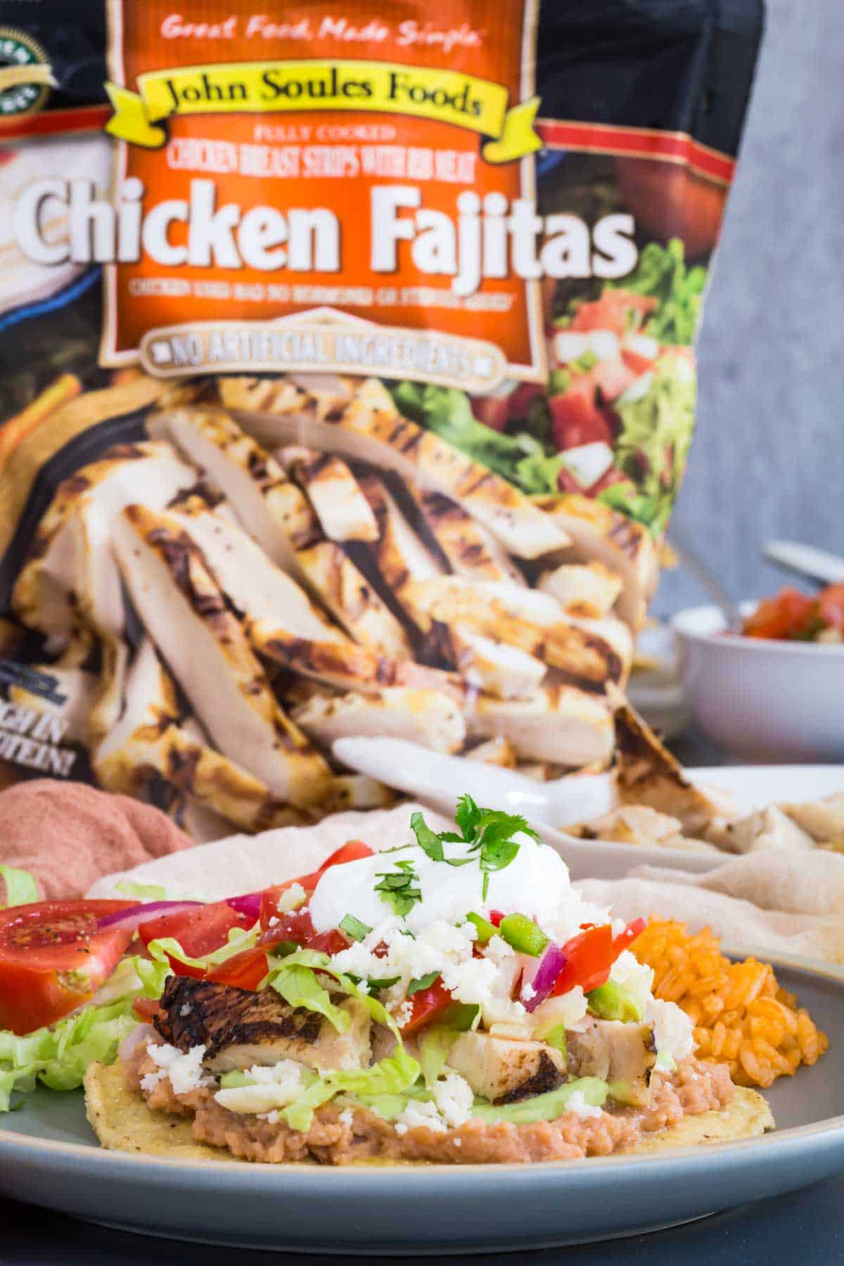 a chicken tostada on a plate with a bag of John Soules Foods fully cooked chicken fajita strips behind it