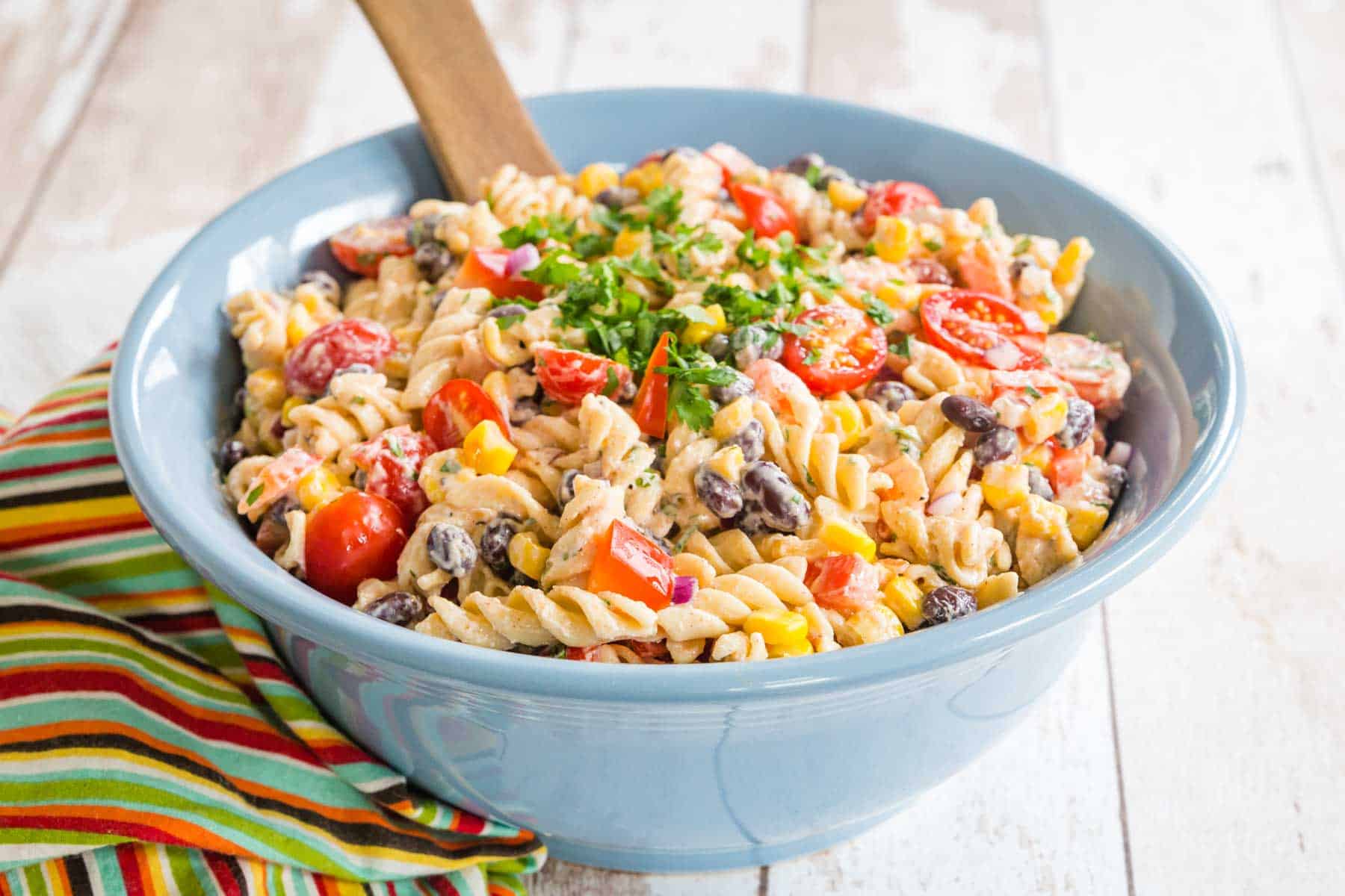 striped napkin on a white picnic table with a blue bowl of mexican macaroni salad