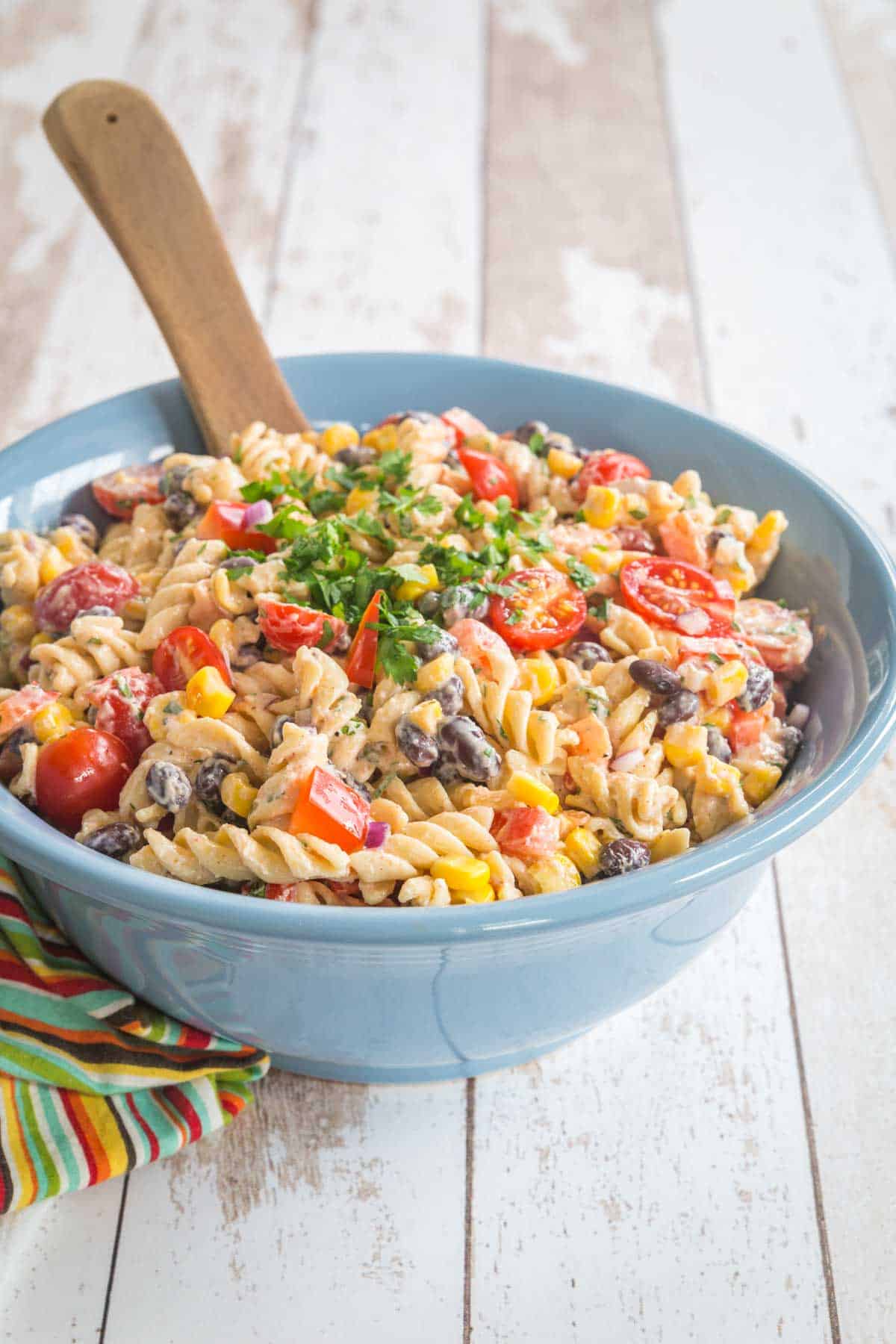 creamy southwestern pasta salad in a blue serving bowl on top of a multicolored striped napkin