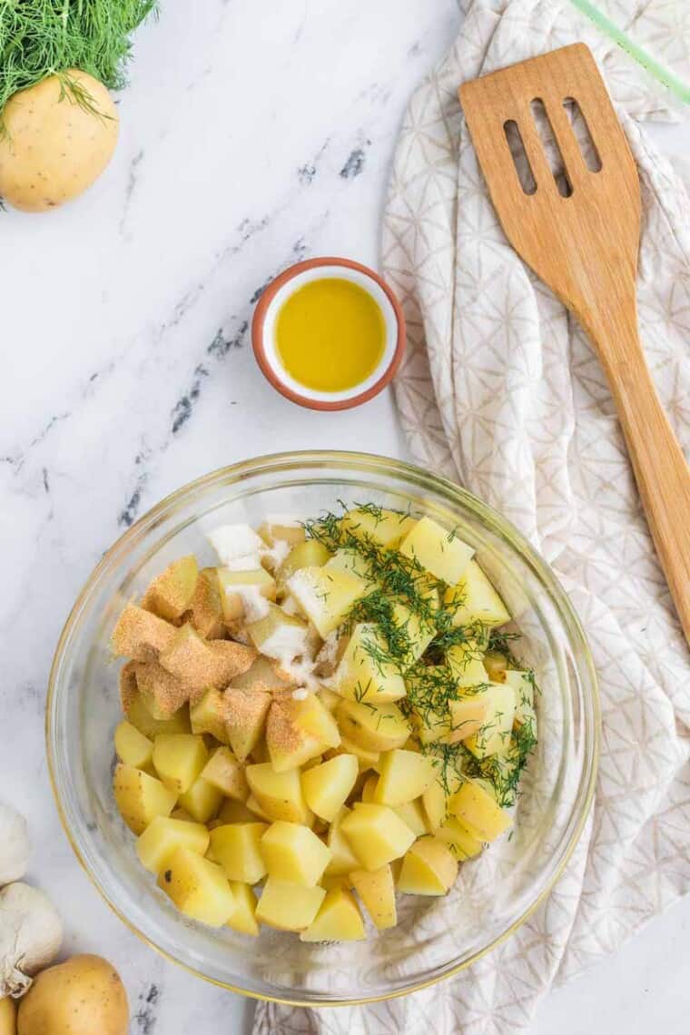 glass bowl of diced potatoes with fresh dill and garlic salt