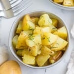 overhead of a whtie bowl with baked dill potatoes and fresh dill on top