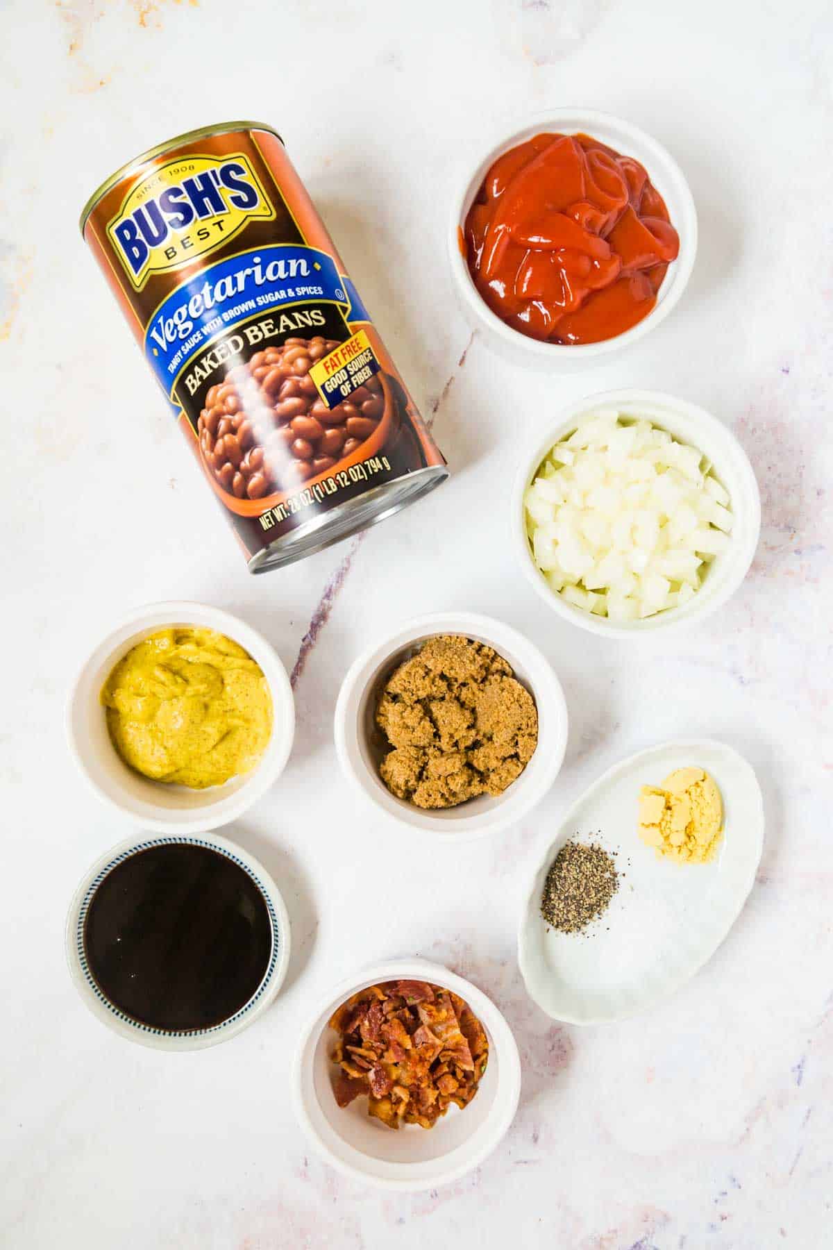 a can of Bush's baked beans and bowls of molasses, crumbled bacon, salt, pepper, dry mustars, brown sugar, spicy brown mustard, and ketchup