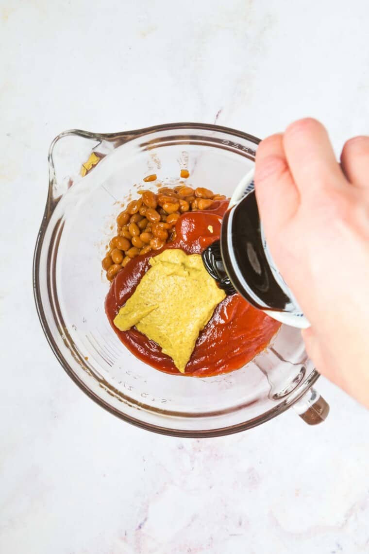 pouring molasses into the bowl with the drained beans, ketchup, and mustard