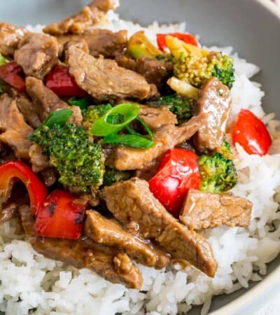 hunan beef stir fry with red peppers and broccoli over white rice in a light blue bowl
