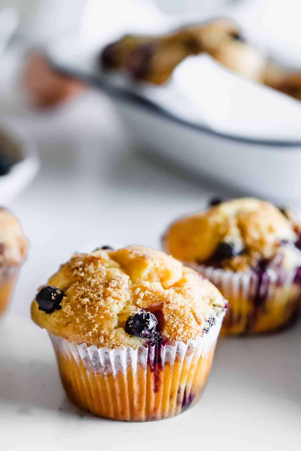 A Single Blueberry Muffin on a White Surface with More Muffins in the Background