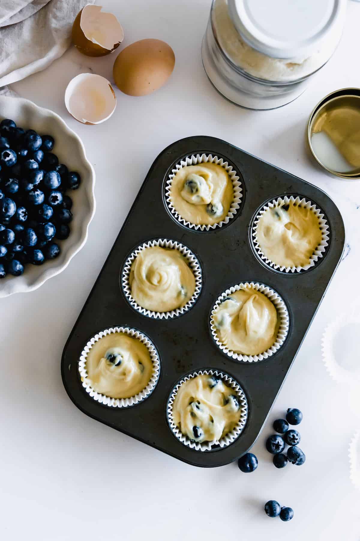 A Muffin Pan Filled with Liners Which are Filled with Blueberry Muffin Batter