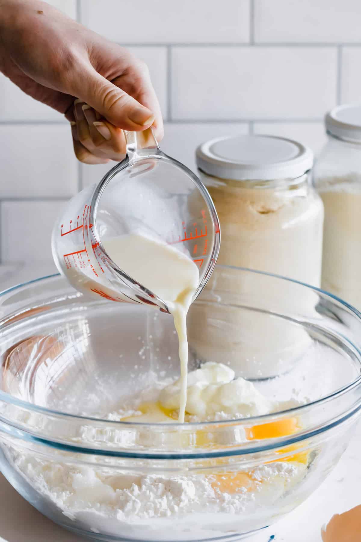 Milk being poured into the pita bread dough mixture in a glass bowl.