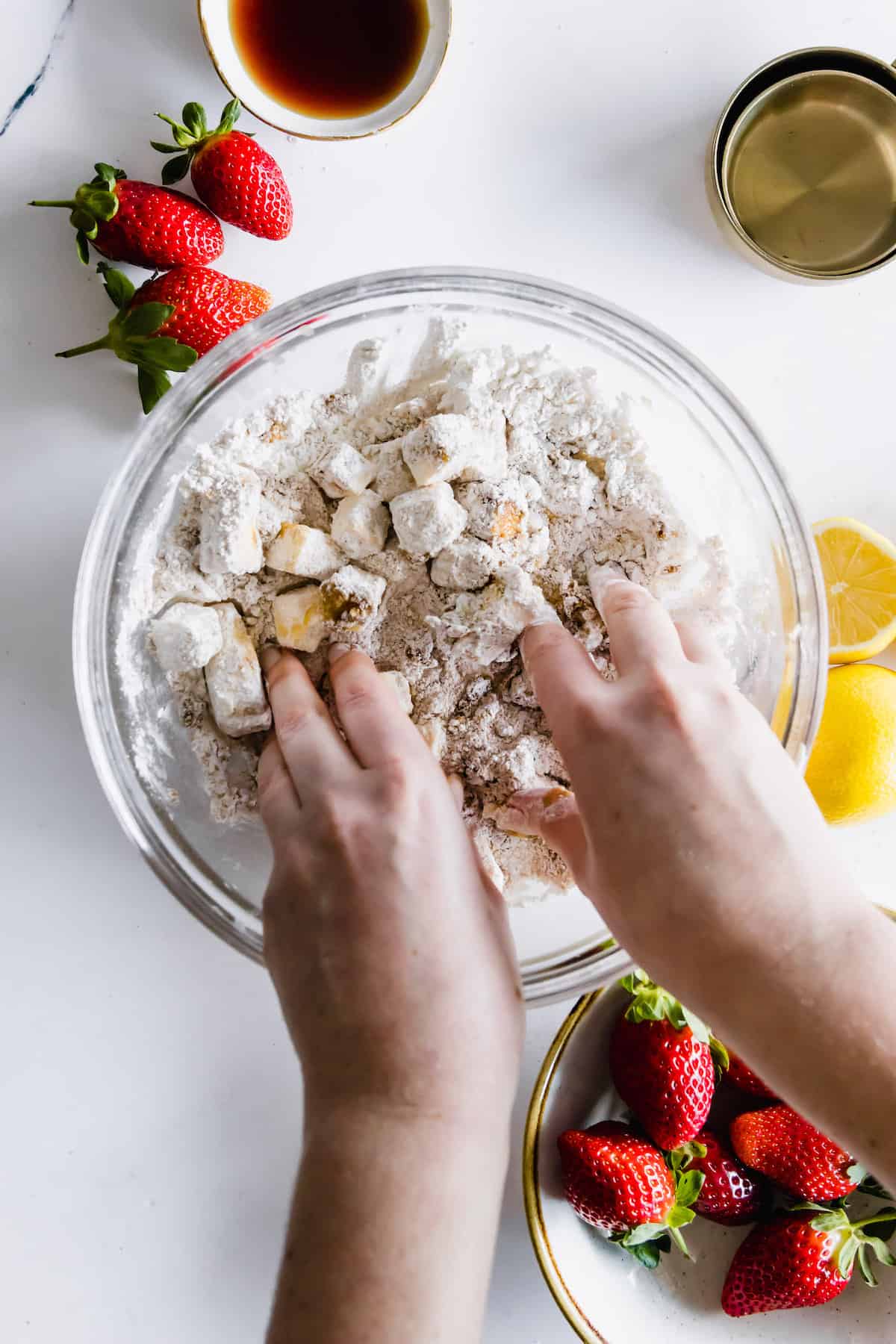 Cubes of cold butter being mixed into the dry topping ingredients by a pair of hands.