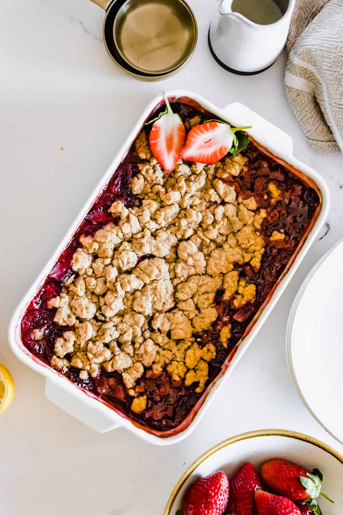 A strawberry crumble in a pan with two sliced strawberries on top.