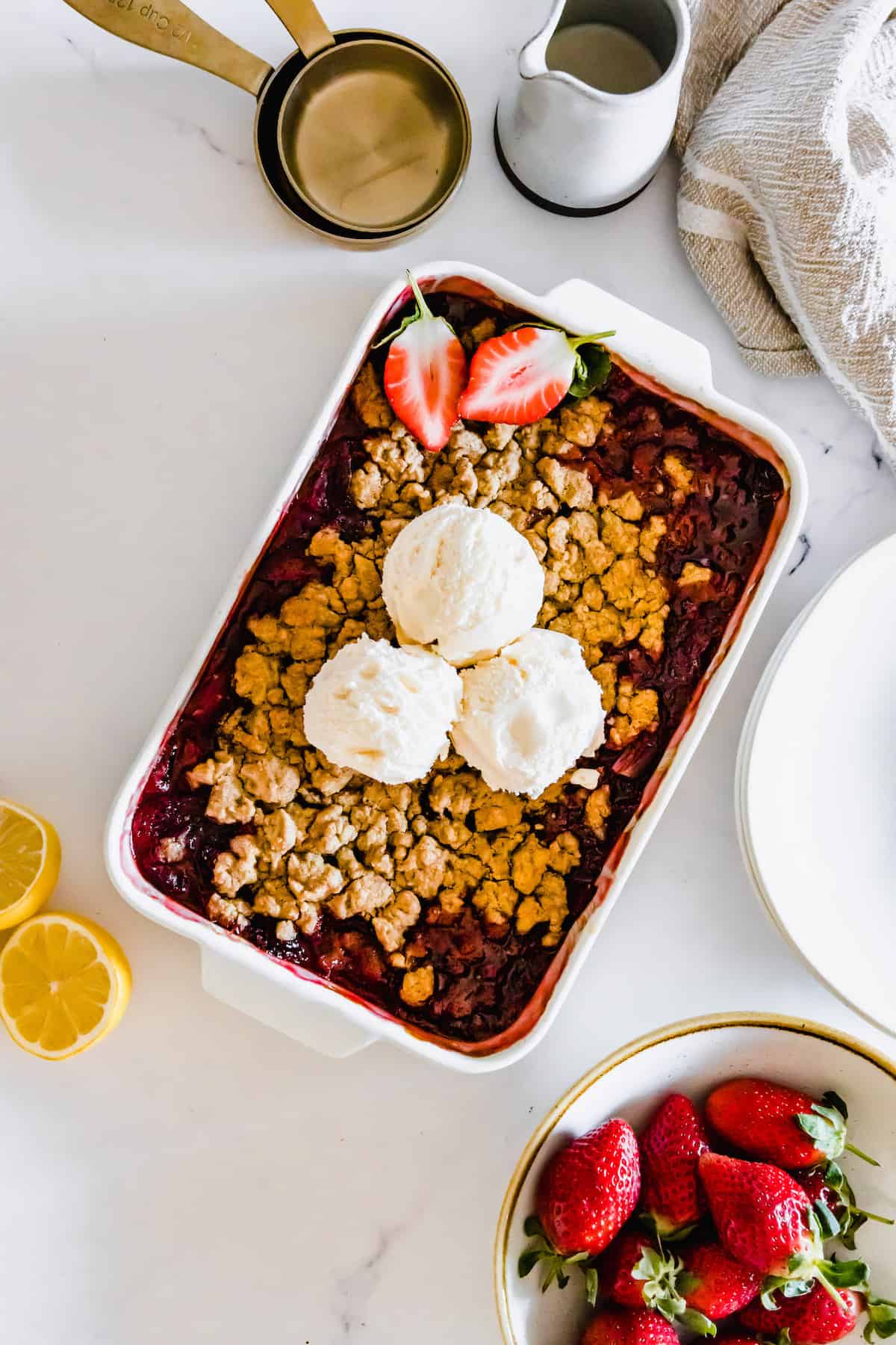 A gluten free strawberry crumble in a white pan topped with three scoops of vanilla ice cream.