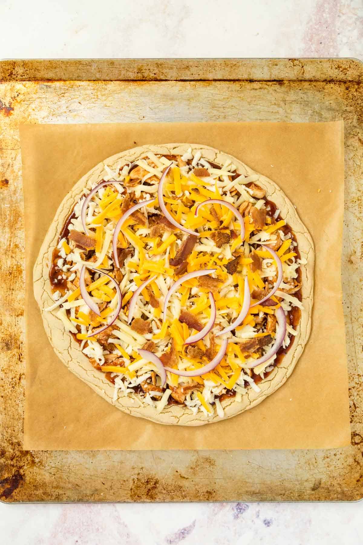 unbaked barbecue chicken pizza on a parchment lined baking sheet