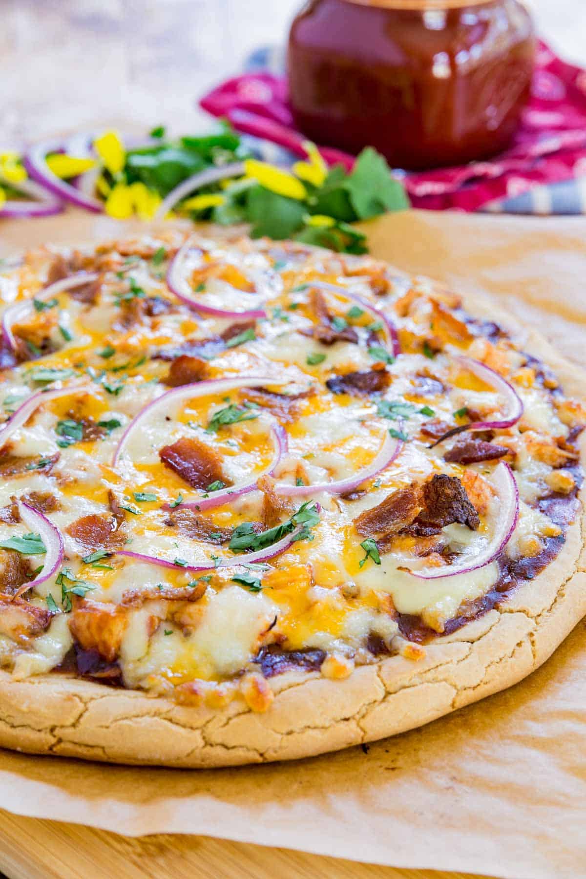 barbecue chicken pizza on a parchment-lined cutting board with a jar of bbq sauce behind it