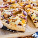 hand using a spatula to get a slice of pizza