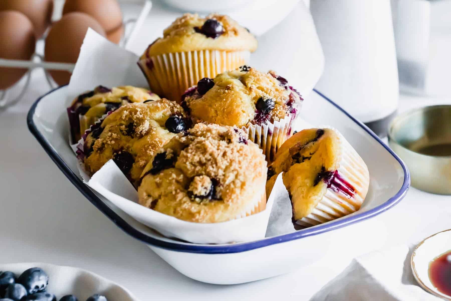 six blueberry muffins piled in a white bowl lined with wax paper