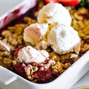 A serving spoon in a strawberry crumble with ice cream on top.