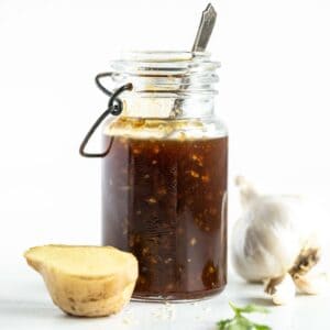 teriyaki sauce in a glass jar with a piece of ginger and a bulb of garlic next to it