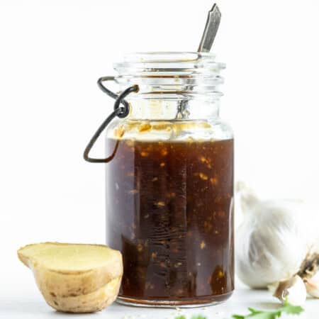 teriyaki sauce in a bottle next to a piece of fresh ginger and a bulb of garlic
