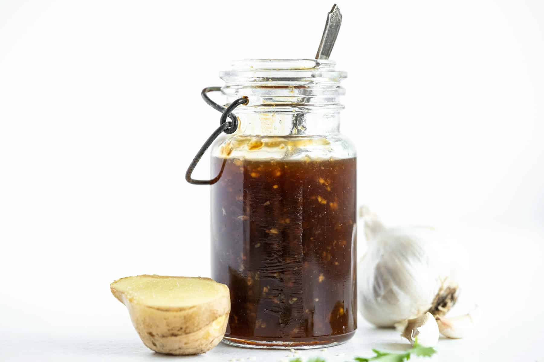 teriyaki sauce in a bottle next to a piece of fresh ginger and a bulb of garlic