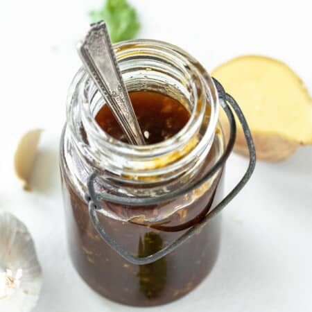 Looking down into a glass bottle of teriyaki sauce with a spoon in it.