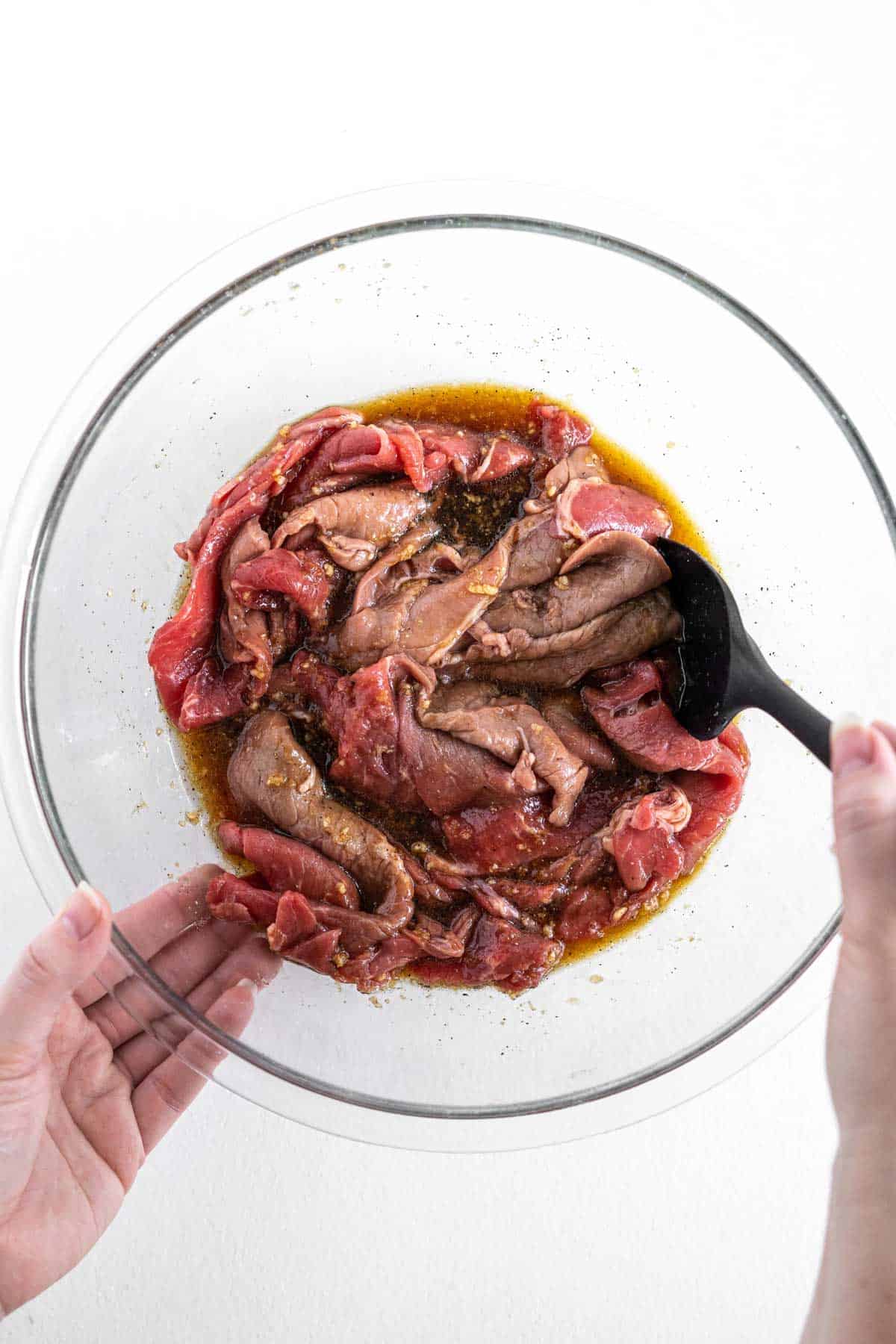 hands marinating sliced meat in teriyaki sauce in a bowl