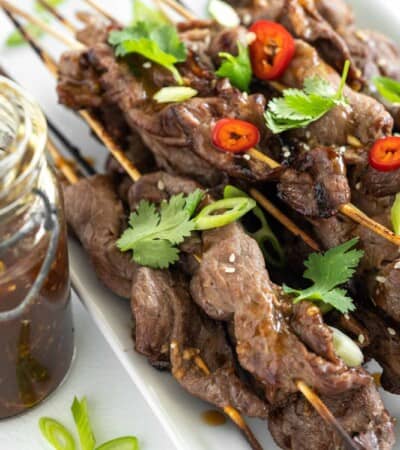 grilled teriyaki steak skewers on a platter with peppers and herbs on top