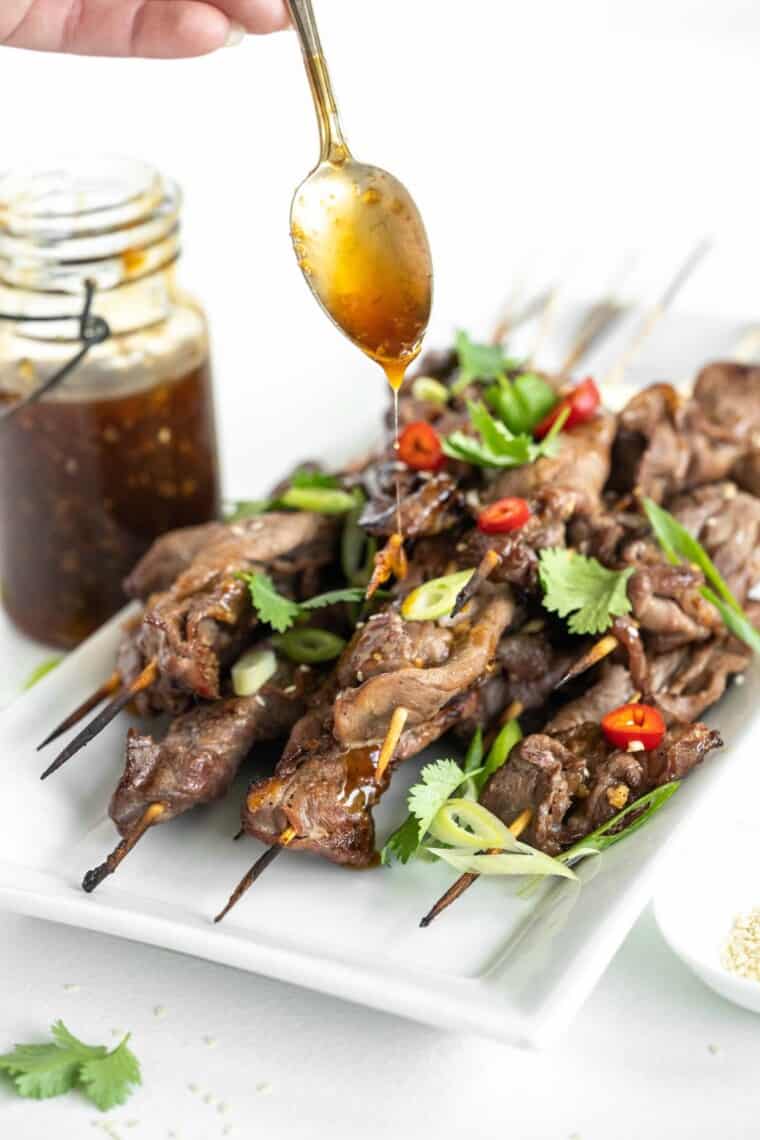 spoon drizzling teriyaki sauce over grilled steak skewers.