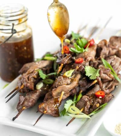 spoon drizzling teriyaki sauce over grilled steak skewers