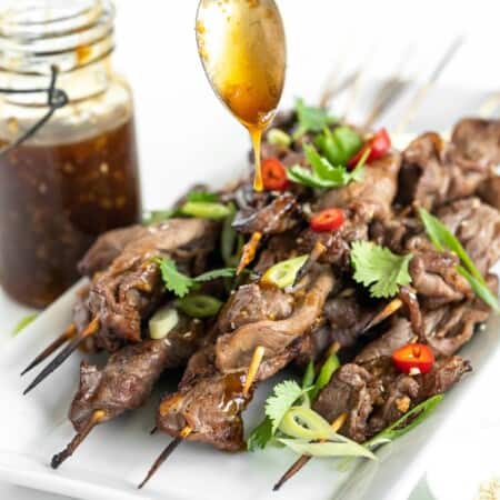spoon drizzling teriyaki sauce over grilled steak skewers
