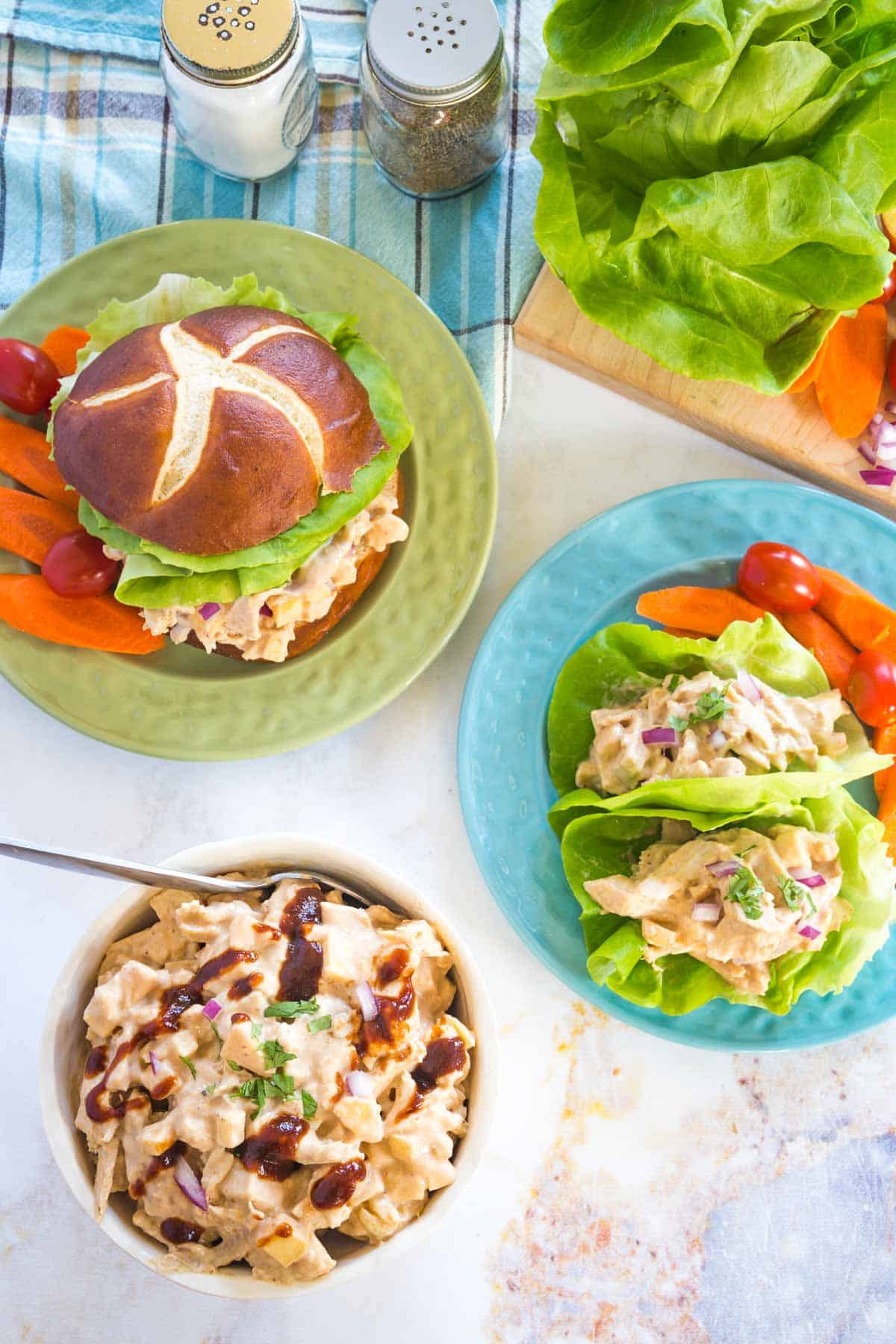 bbq chicken salad in a bowl, a barbecue chicken salad sandwich on a green plate and lettuce wraps on a blue plate