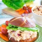 barbecue chicken salad sandwich on a roll with carrots and tomatoes on the side on a green plate