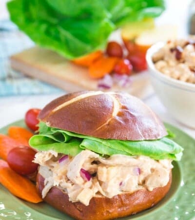 barbecue chicken salad sandwich on a roll with carrots and tomatoes on the side on a green plate