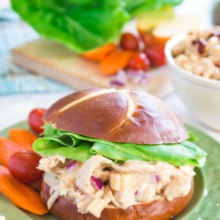 barbecue chicken salad sandwich on a roll with carrots and tomatoes on the side on a green plate