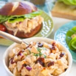 a bowl of barbecue chicken salad with a sandwich on a plate in the background