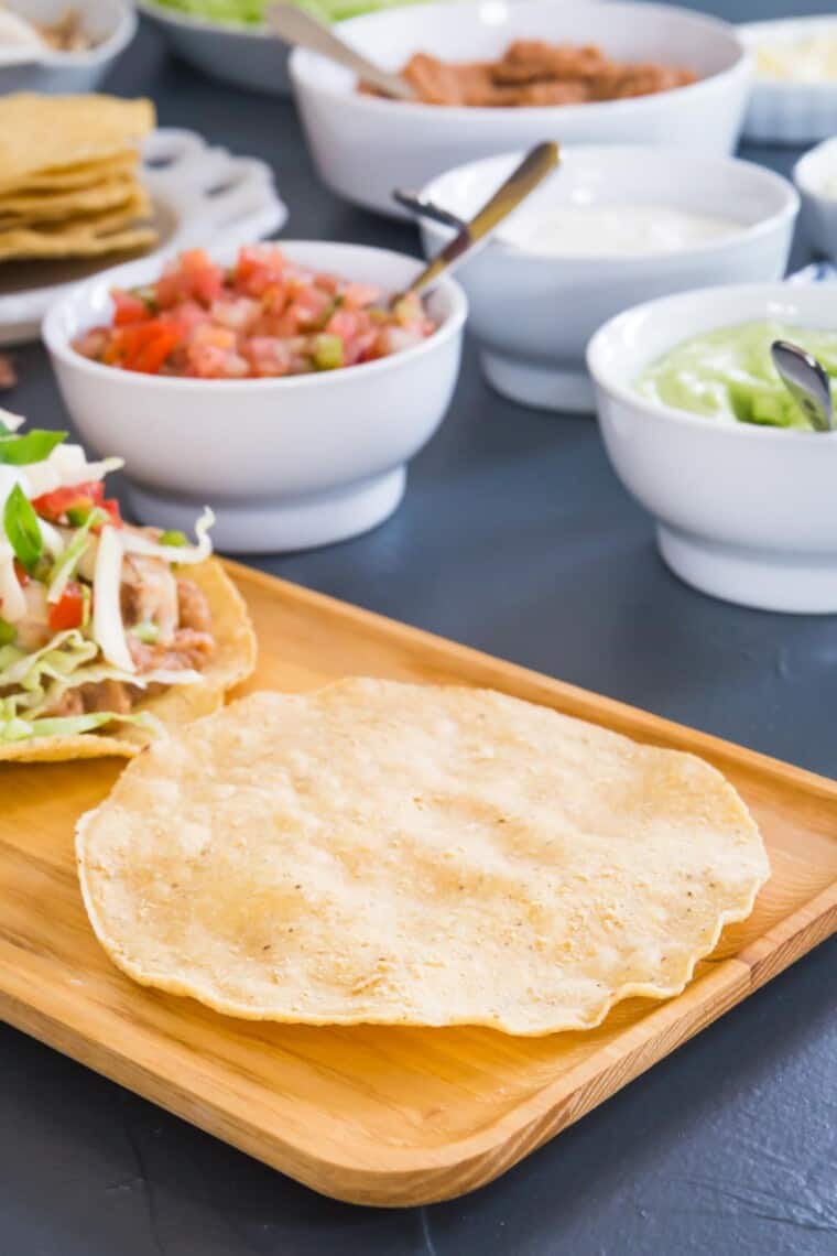 an empty tostada shell on a platter with bowls of toppings behind it