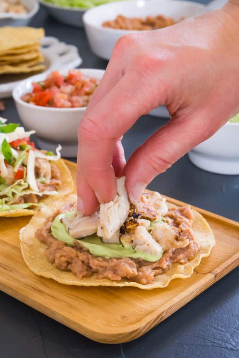 hand placing chicken on top of the tostada