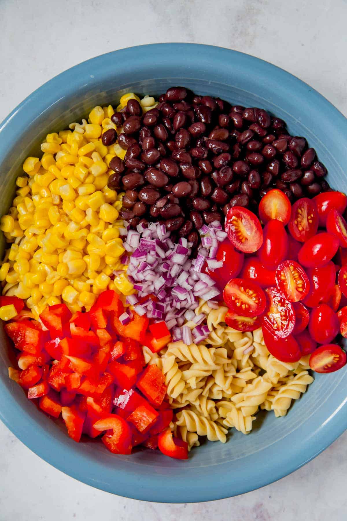 bowl of cooked pasta topped with red pepper, black beans, corn, halved grape tomatoes, and minced red onion