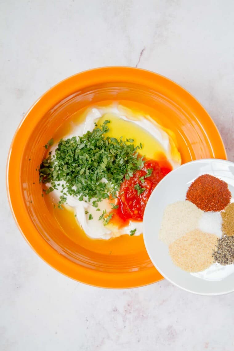 southwestern dressing ingredients in an orange bowl with the spiced being poured in from a white plate