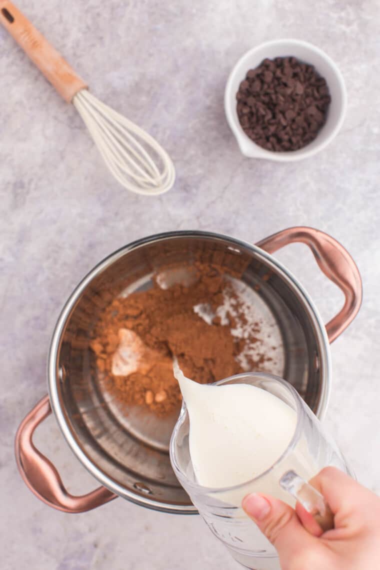 pouring heavy cream into a small pot with cocoa powder and corn syrup