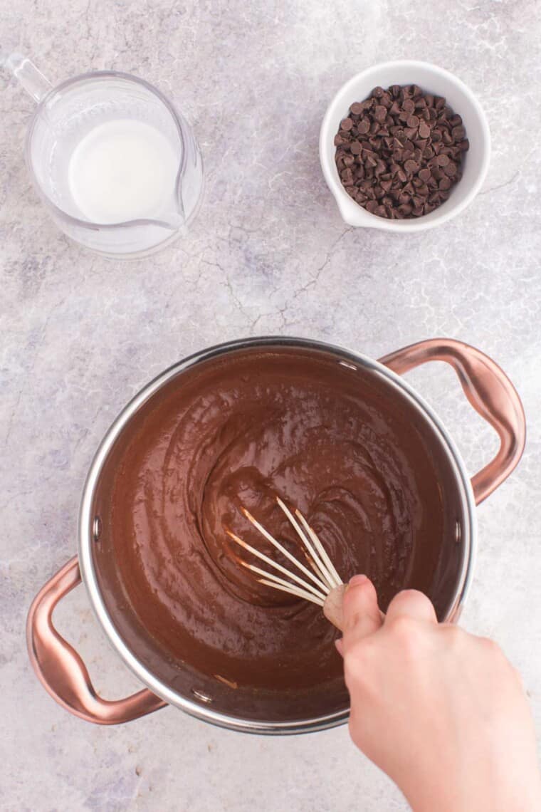 whisking the fudge sauce in a pot with the bowl of chocolate chips next to it