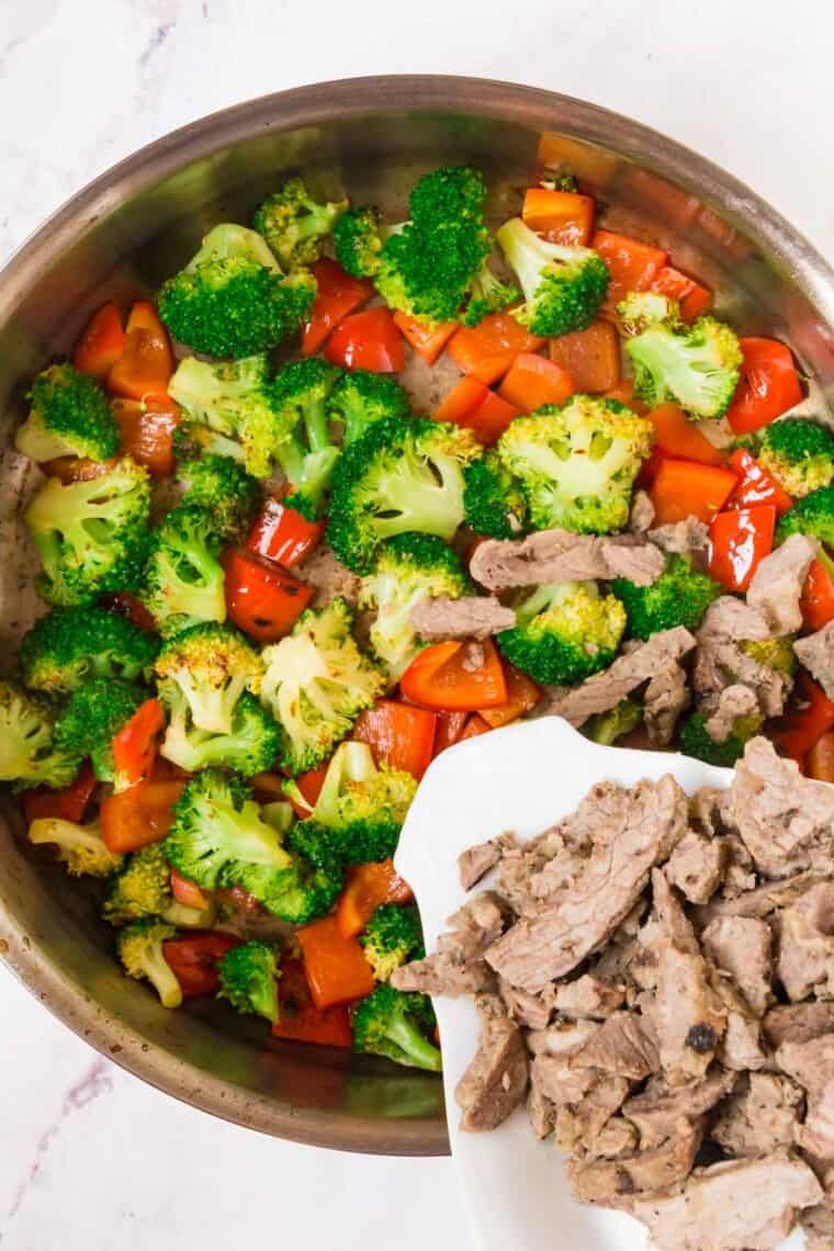 adding steak slices to the broccoli and peppers in the skillet