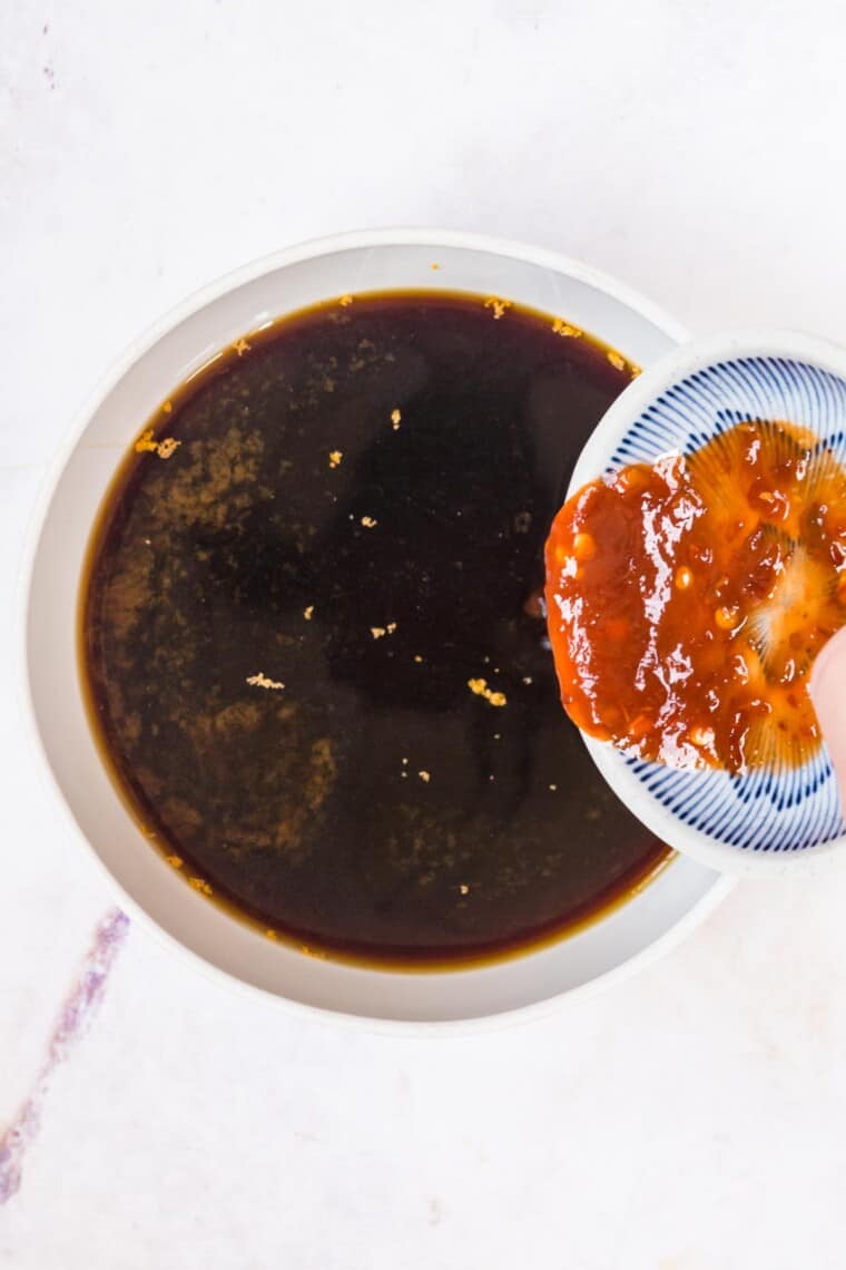 adding chili paste to a bowl of beef broth and soy sauce