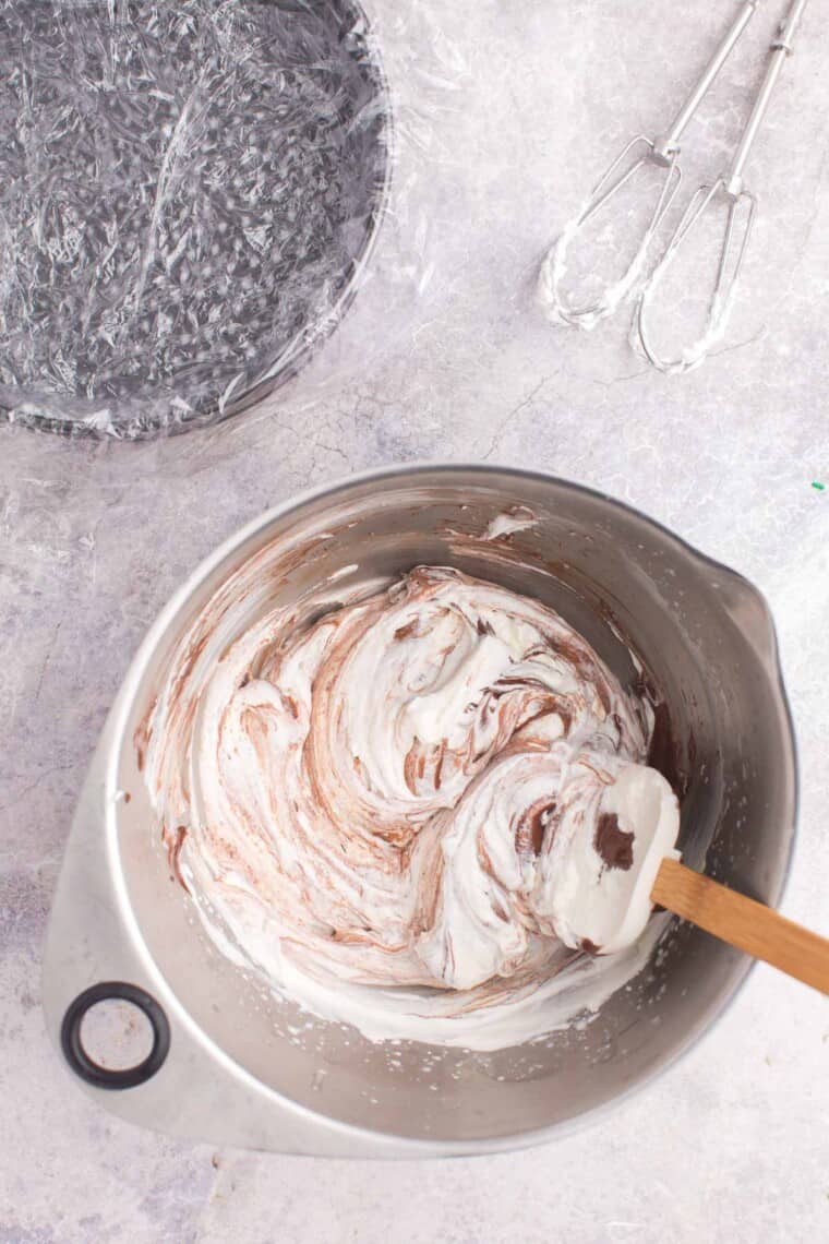chocolate mixture being folded into whipped cream in a large bowl
