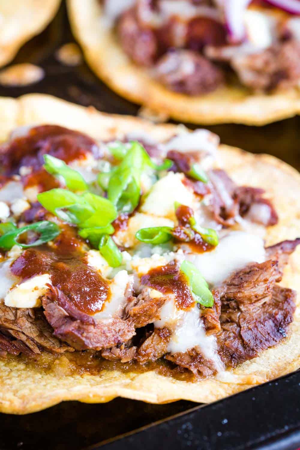 crispy corn tostada shell topped with slices of beef in steak sauce, melted monterey jack and blue cheese, topped with more steak sauce and sliced green onions