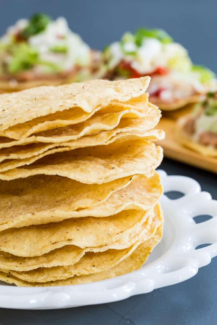 stack of tostada shells on a white plate with chicken tostadas in the background