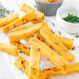 baked polenta fries spread around ona piece of parchment paper and a small dish of dipping sauce