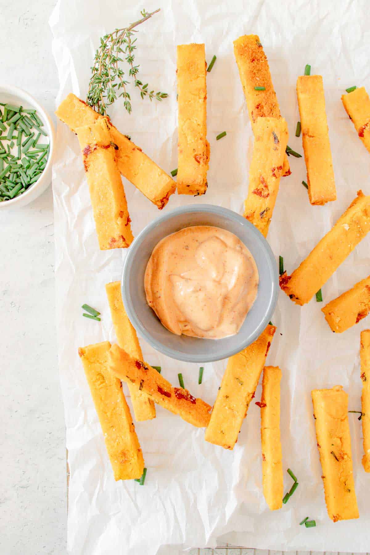 a small bowl of chipotle aioli on a piece of parchment paper surrounded by polenta fries and minced chives