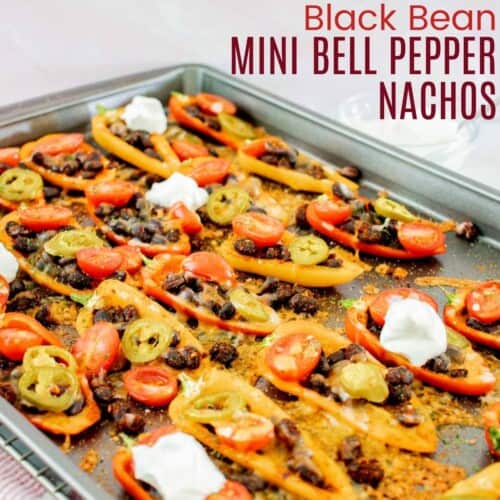 a sheet pan with baked bell pepper nachos with black beans, tomatoes, jalapeno slices, melted cheese, and dollops of sour cream on several