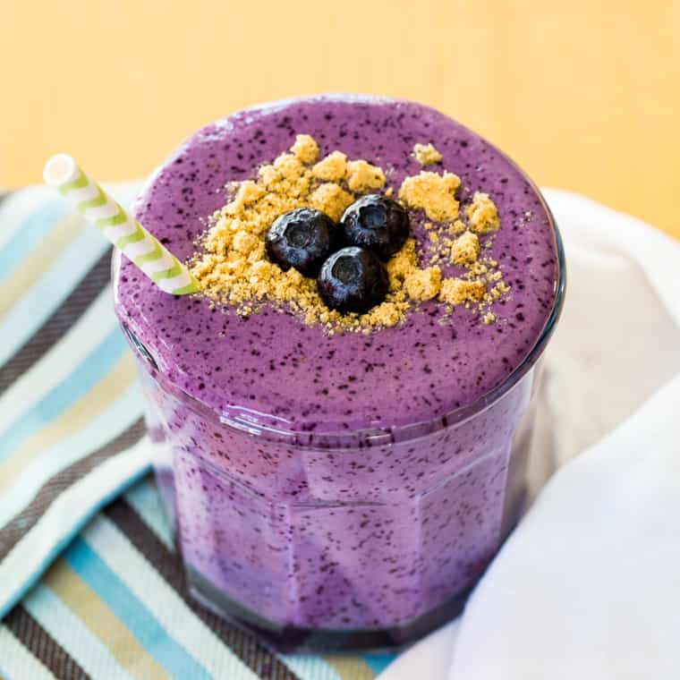 A blueberry yogurt smoothie in a glas with blueberries and graham cracker crumbs on top.